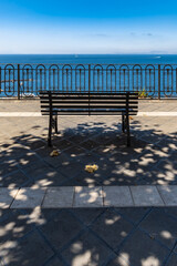 Fototapeta na wymiar Small bench standing on the edge in front of metal railing with beautiful view to the sea
