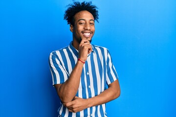 Fototapeta na wymiar Young african american man with beard wearing casual striped shirt looking confident at the camera with smile with crossed arms and hand raised on chin. thinking positive.