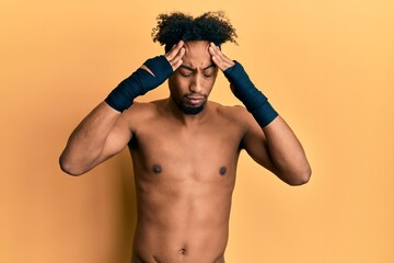 Young african american man with beard using boxing protection with hand on head, headache because...
