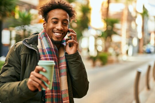 Young african american man talking on the smartphone and drinking coffee at the city