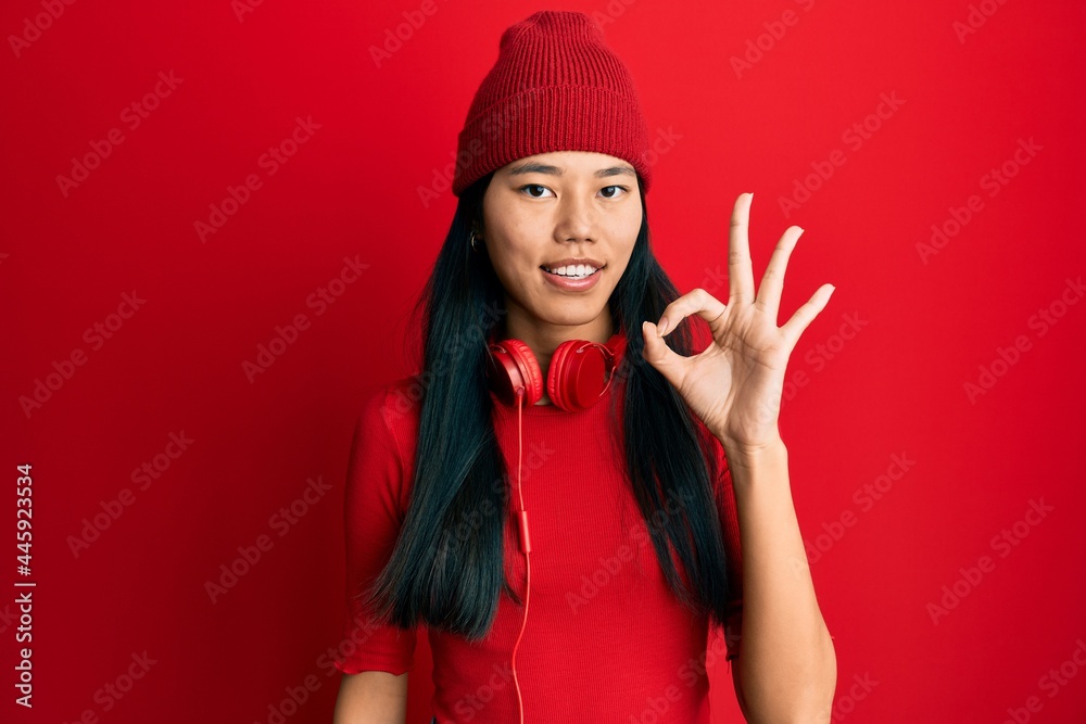 Sticker young chinese woman listening to music using headphones smiling positive doing ok sign with hand and