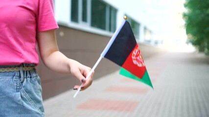 Unrecognizable woman holding Afghan flag. Girl walking down street with national flag of Afghanistan