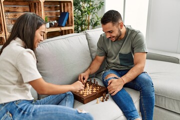Young latin couple smiling happy playing chess at home.