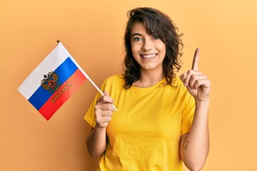 Young hispanic woman holding russia flag smiling with an idea or question pointing finger with happy face, number one