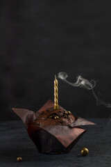 Festive concept. Extinguished golden candle on a delicious chocolate muffin with powdered sugar on...