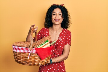 Young latin girl holding picnic wicker basket with bread smiling and laughing hard out loud because...