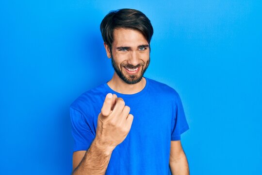 Young hispanic man wearing casual clothes beckoning come here gesture with hand inviting welcoming happy and smiling