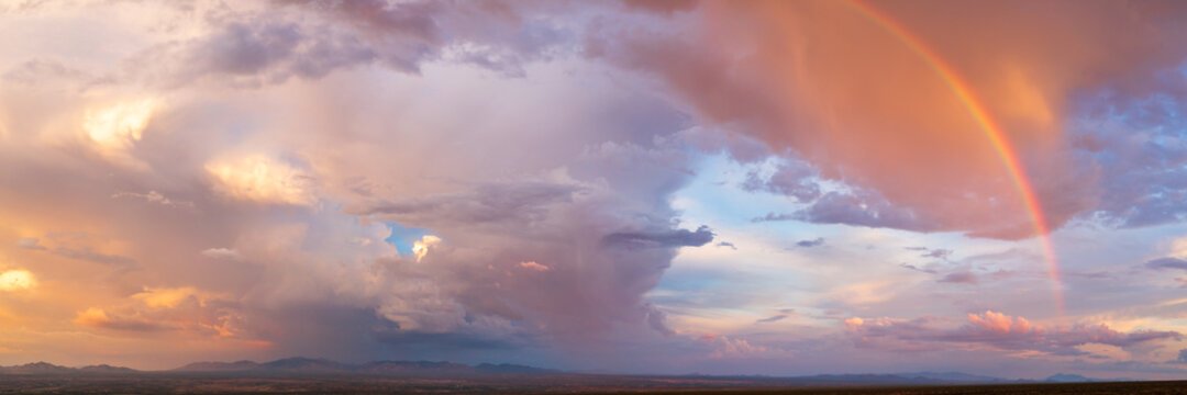 Dramatic aerial panorama of a storm with setting sun and rainbow in the American Southwest.