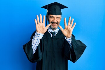 Middle age hispanic man wearing graduation cap and ceremony robe showing and pointing up with fingers number ten while smiling confident and happy.