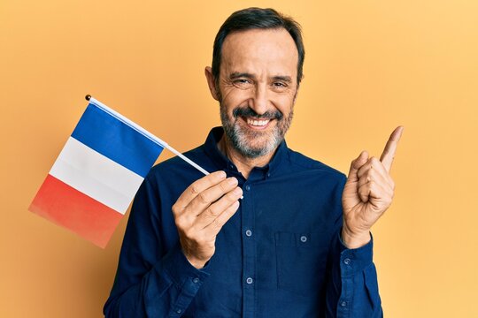 Middle age hispanic man holding france flag smiling happy pointing with hand and finger to the side