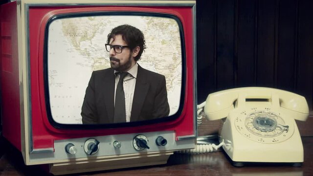 A transmission in an old television set near a rotary phone: a man in an elegant suit acting silly around a world map (a funny mad broadcast weather report).
