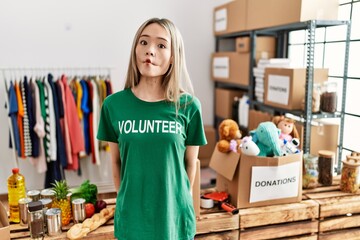 Asian young woman wearing volunteer t shirt at donations stand making fish face with lips, crazy and comical gesture. funny expression.