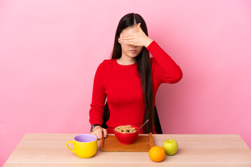 Young Chinese girl  having breakfast in a table covering eyes by hands. Do not want to see something