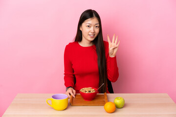 Young Chinese girl  having breakfast in a table happy and counting four with fingers