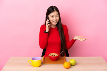 Young Chinese girl  having breakfast in a table keeping a conversation with the mobile phone with someone