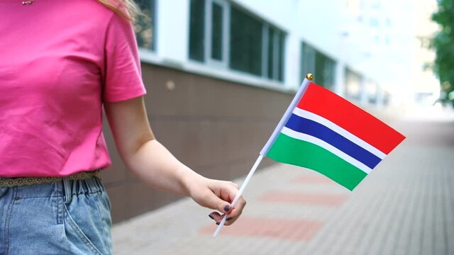 Unrecognizable woman holding Gambian flag. Girl walking down street with national flag of Gambia