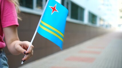 Unrecognizable woman holding Aruban flag. Girl walking down street with national flag of Aruba