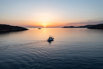 Fototapeta na wymiar Fishing boat at sunset. Greece. Aerial drone view of typical fishing boat moving on calm sea and orange color sky background.