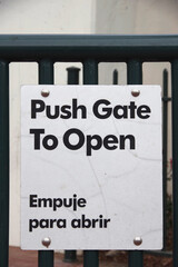 Bilingual sign “Push Gate To Open” on the gate to a public park