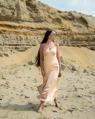 a beautiful young girl with long flowing hair walks along the sand dunes against the background of...