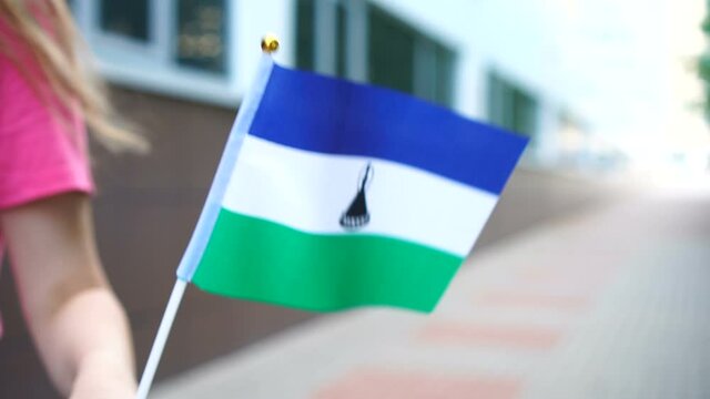 Unrecognizable woman holding Basotho flag. Girl walking down street with national flag of Lesotho