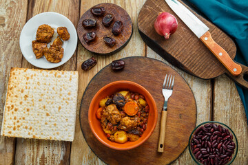 Jewish dish chelnt with meat on the table in a plate near ingredients and matzo.