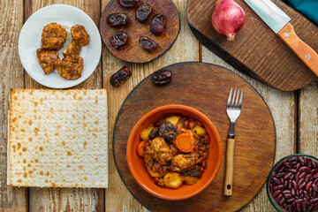 Jewish dish chelnt with meat on the table in a plate near ingredients and matzo.