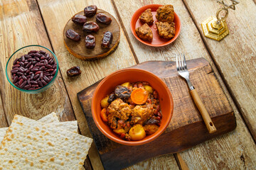 Jewish dish shuttle with meat in a clay dish on a wooden table near matzo and ingredients.