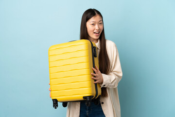 Young Chinese girl over isolated background in vacation with travel suitcase and surprised