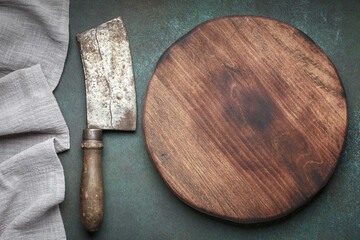 Round cutting board with meat cleaver on dark background, top view with copy space for text