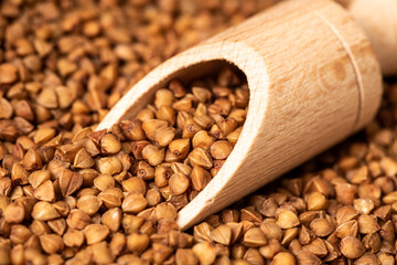 Obraz premium A wooden ladle lies on a brown buckwheat. Close-up.