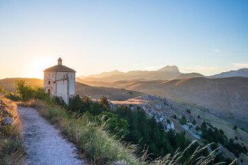 The small octagonal chapel near Rocca Calascio castle ruins at sunset in backlight, landmark in the Gran Sasso National Park, Abruzzo, Italy. Mountains scenic background.