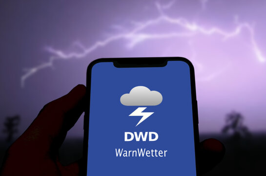 Logo der DWD WarnWetter App wird auf einem Smartphone angezeigt, im Hintergrund der Blitz eines n&auml;chtlichen Gewitters, Unwetter, Unwetterwarnung, Extremwetter