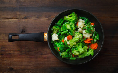 Fried vegetables in pan on wood table background. Flat lay.