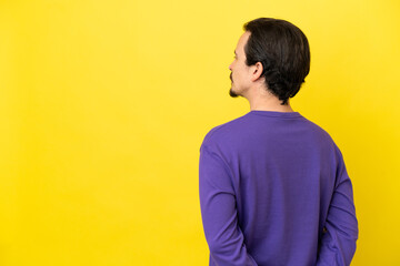 Young caucasian man isolated on yellow background in back position and looking back