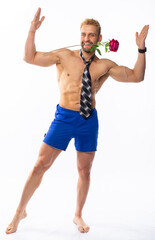 Fototapeta premium a muscular man in blue shorts and a tie holds a rose in his teeth, raised his hands up. isolated, white background