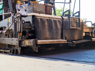 Close-up back view of an road paver in the process of paving asphalt.