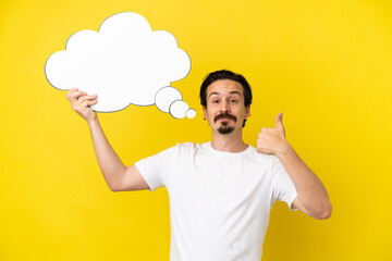 Young caucasian man isolated on yellow background holding a thinking speech bubble with thumb up