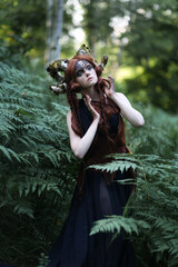 Beautiful red haired girl faun with dark makeup and mossy horns among fern
