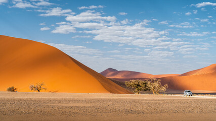 Tourist vehicle next to towering sand dunes in the Namib desert near Sossusvlei, Namib-Naukluft National Park, Namibia, Africa.