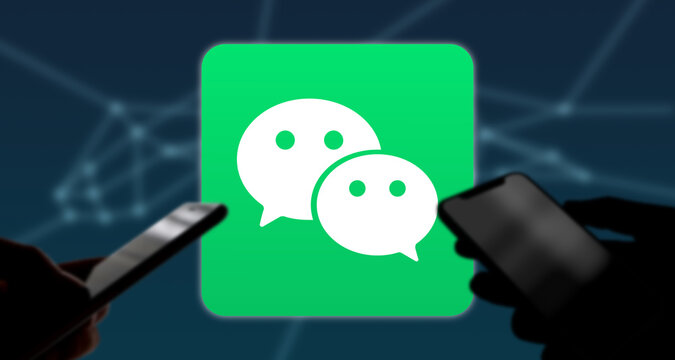 Zwei Personen halten Smartphone in der Hand, im Hintergrund das WeChat App Logo, Chat-Dienst, Mobile Payment, China