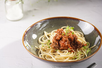 Italian spaghetti with bolognese tomato sauce and fresh thyme in dark green bowl on white concrete surface, with olive oil and balsamic vinegar in the back
