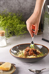 A hand holding a fork with spaghetti with bolognese meat tomato sauce in green bowl garnished with thyme