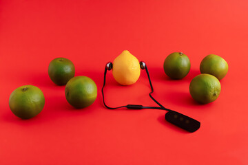 Green and yellow citrus fruit, lemon with a headset and standing out from the group of limes, on red background