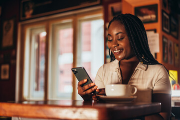 Beautiful young african american woman using smartphone while sitting in a cafe