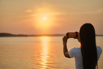 Young woman making photo of sunset with her phone