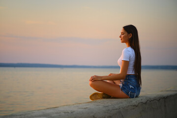Fototapeta na wymiar Side view of a woman in meditation pose on the pier during sunset