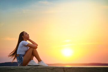 Fototapeta na wymiar Dreamy woman sitting in profile on a pier enjoying the sunset