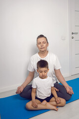 Fototapeta na wymiar grandmother and her grandson are sitting on a yoga mat in a white apartment at home and meditating in the lotus position