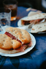 Traditional Italian food. Crispy panini and piadina sandwiches with prosciutto (speck), cheese, lettuce and vegetables with fresh drinks on a table with a blue tablecloth. Healthy European snack.